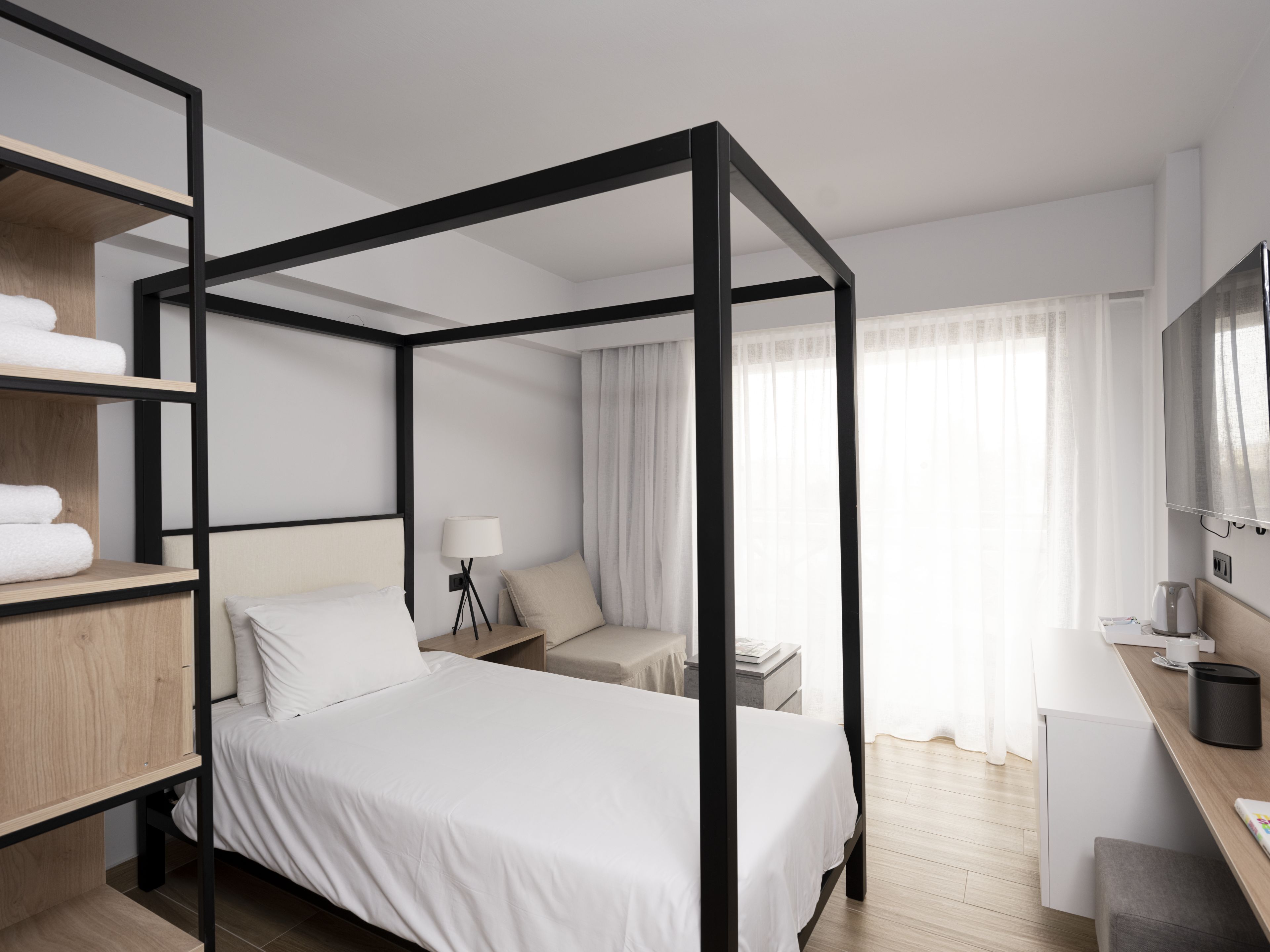 Une chambre d’hôtel moderne dotée d’un lit à baldaquin, d’un bureau avec une chaise, d’une télévision et d’un petit coin salon avec une table et une chaise.
