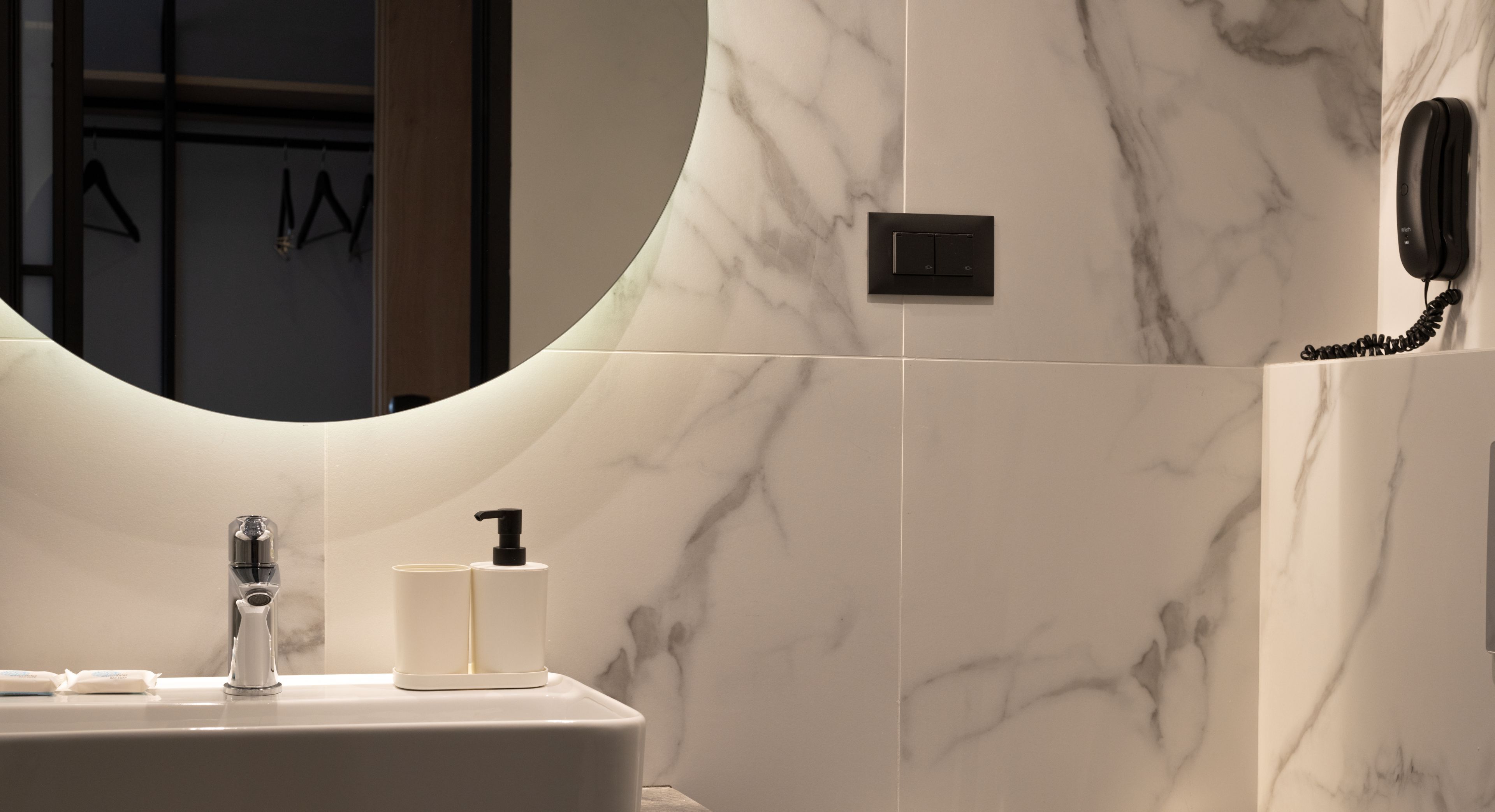 A bathroom with a marble wall, a sink with a faucet, a soap dispenser, and a telephone mounted on the wall.