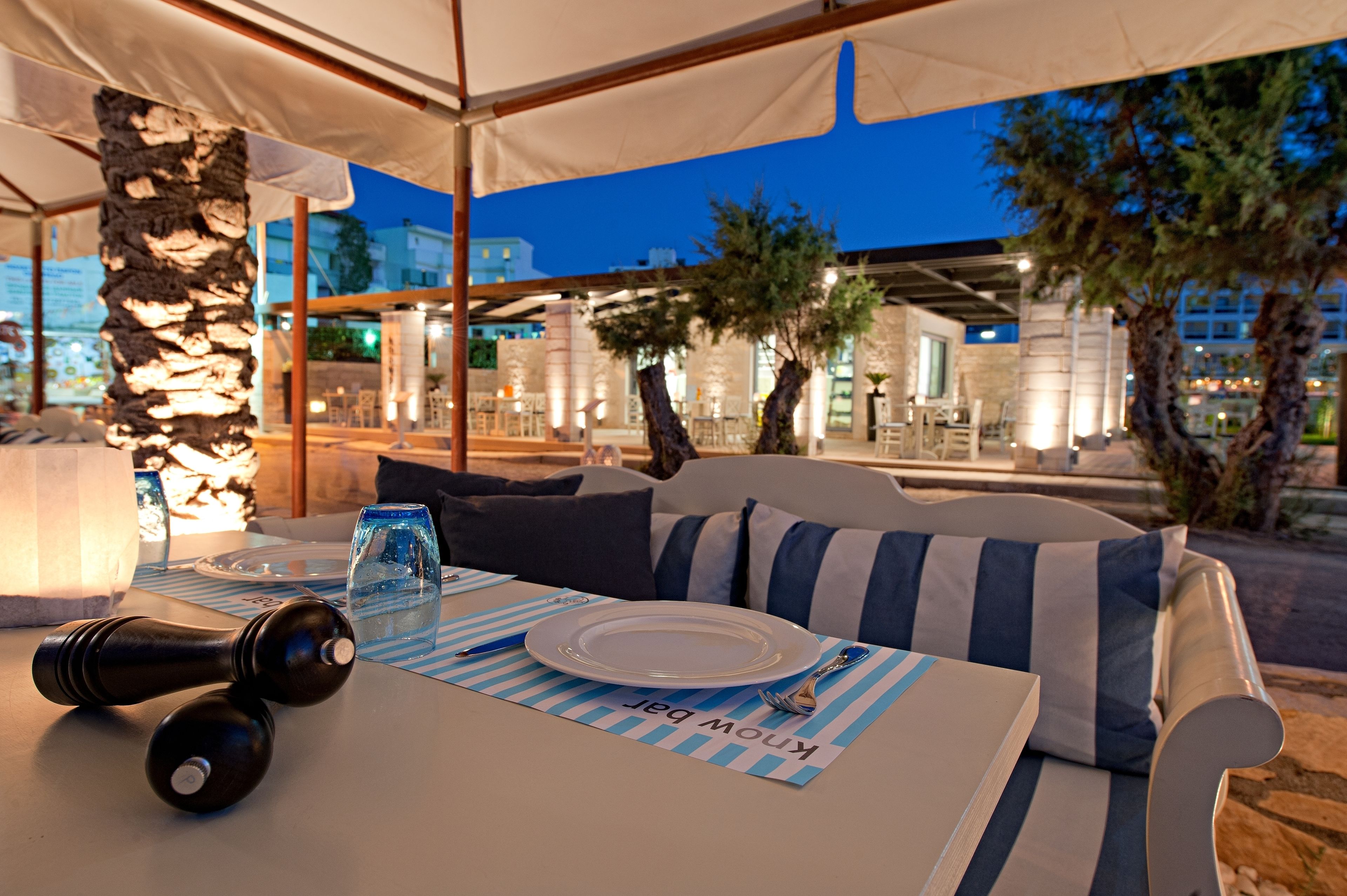 An outdoor dining area with a table set for two, featuring striped tablecloths and a menu card.