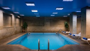 Une piscine intérieure à l’eau claire, entourée de chaises longues avec des serviettes et agrémentée de plantes en pot.