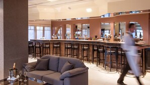 Un espace bar moderne comprenant un comptoir, de nombreux tabourets et un coin salon avec un canapé et une table en verre.