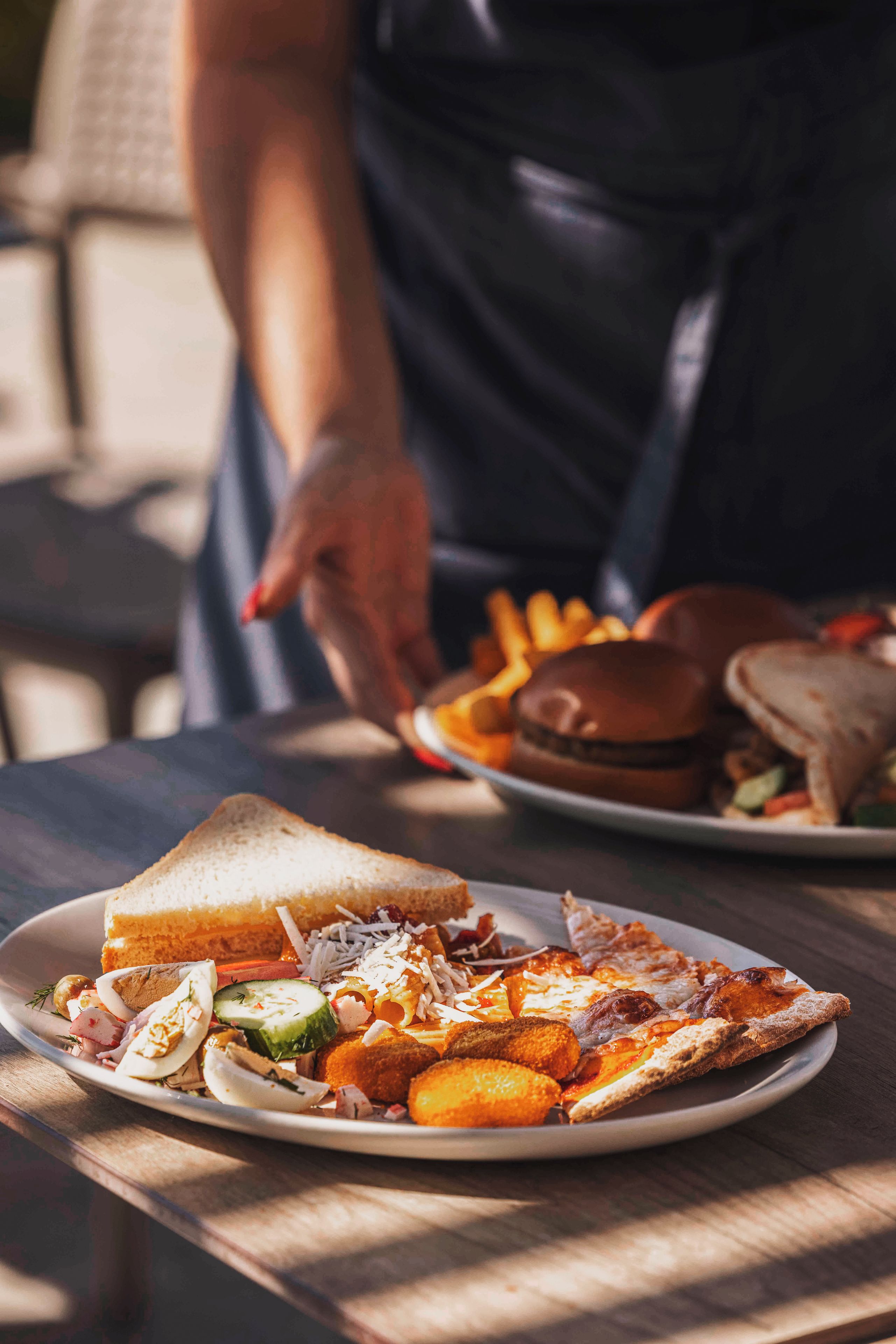 A meal on a wooden table with a sandwich, pizza, fries, and a burger.