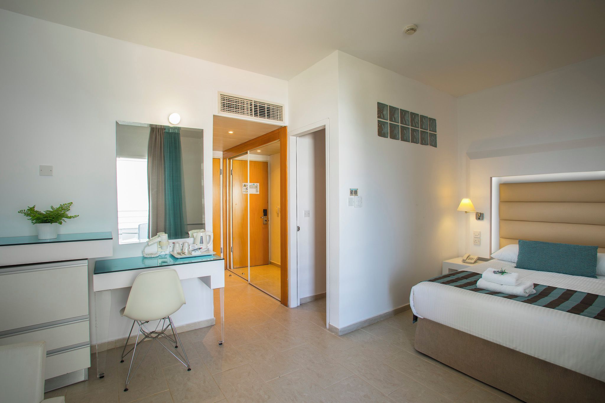 Een hotelkamer met een bed, een bureau, een stoel en een badkamer die door een geopende deur zichtbaar is.