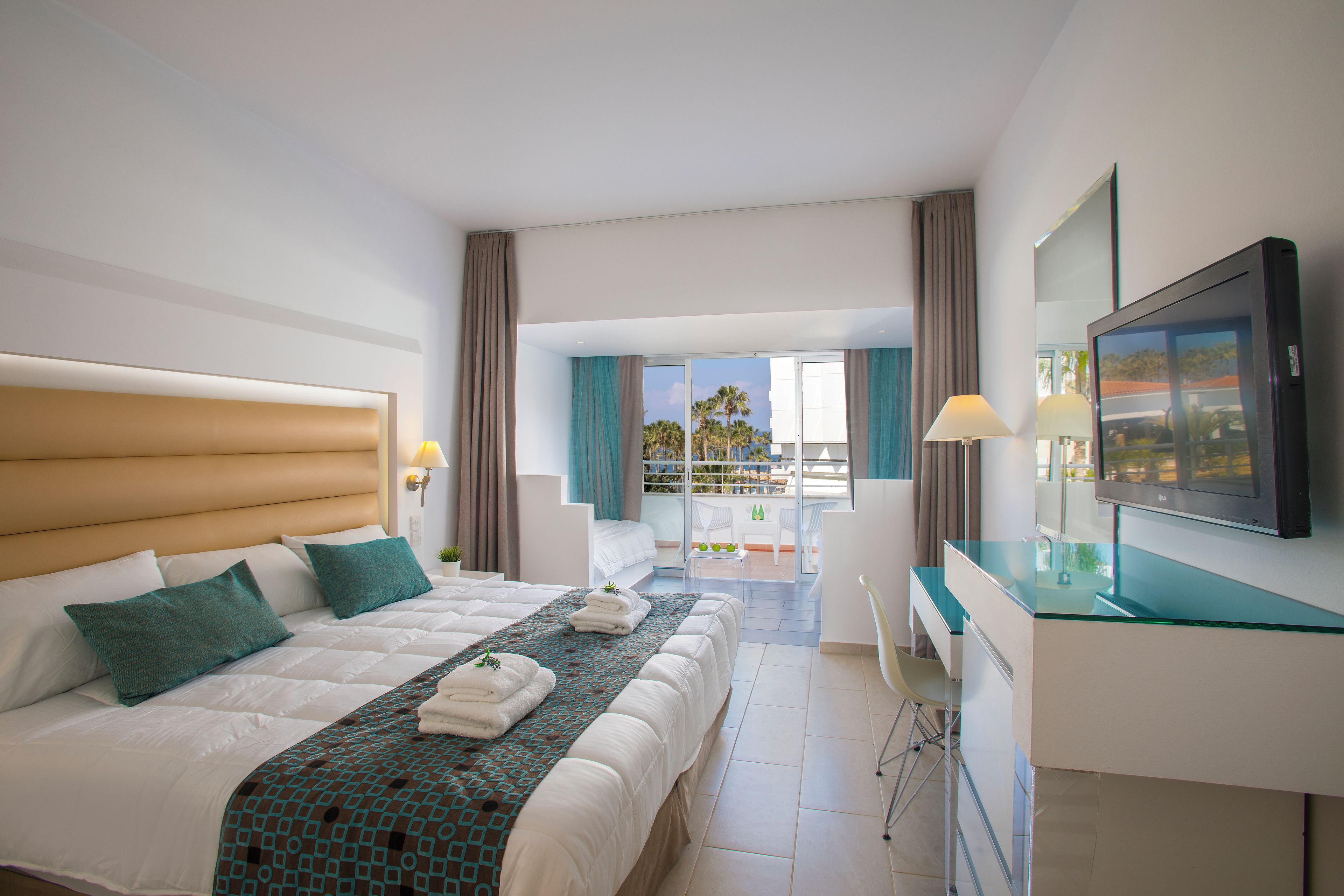 Une chambre d’hôtel avec un lit, un bureau, une télévision et un balcon offrant une vue.
