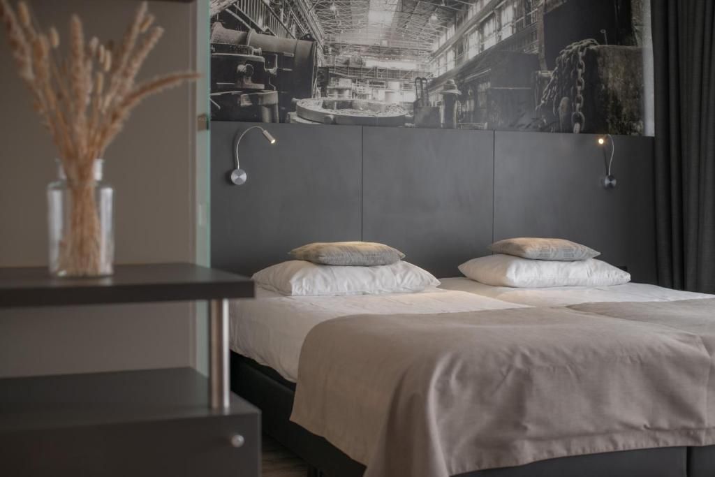 Un dormitorio moderno con una cama grande, dos almohadas, una mesita de noche con un florero y una lámpara de pared.