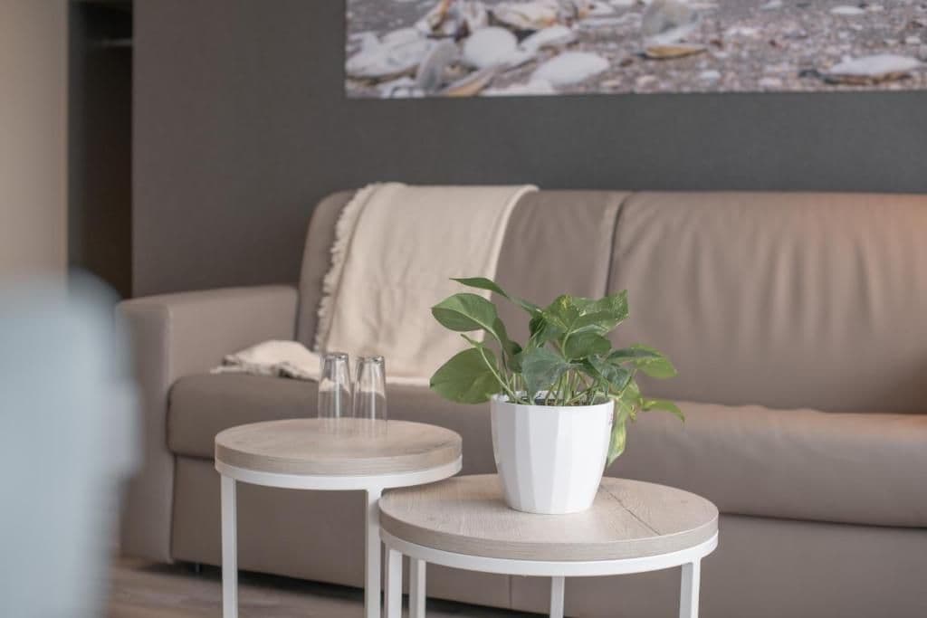 Ein Wohnzimmer mit einem beige gefärbten Sofa, zwei runden weißen Tischen und einem Blumentopf.