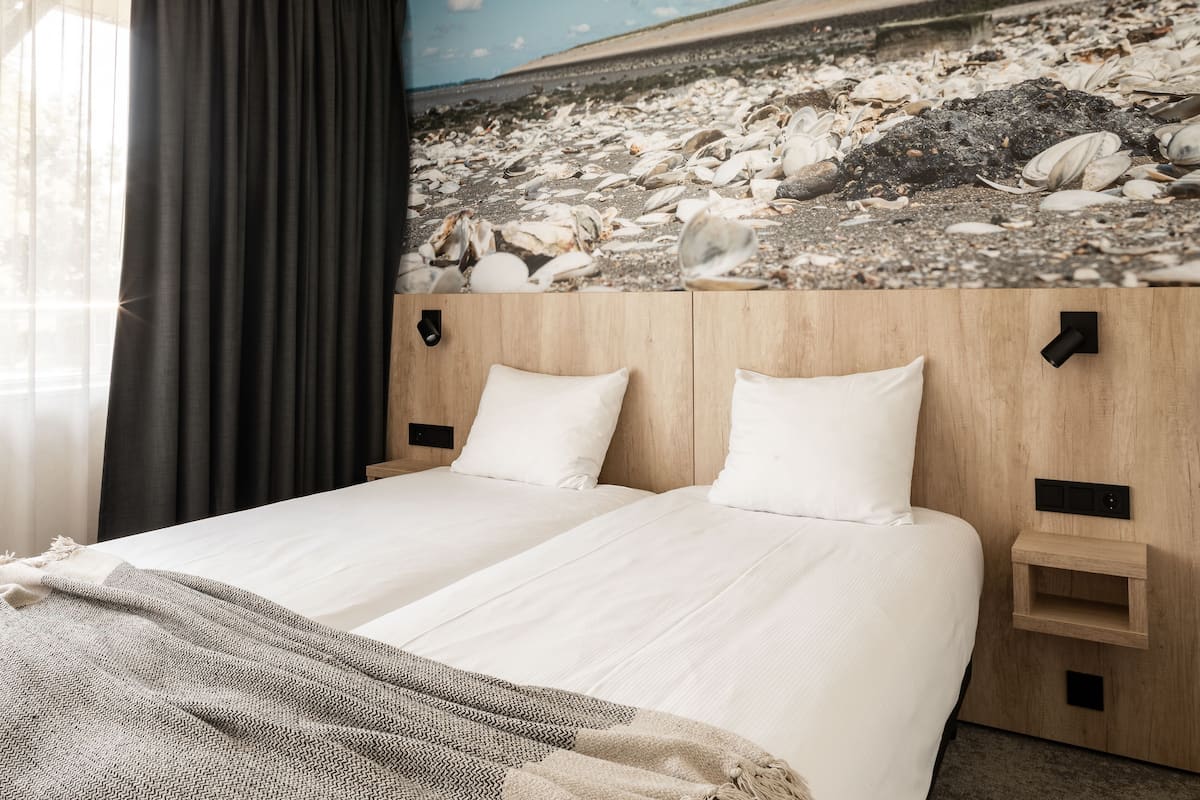 Un lit double avec du linge de lit blanc, une tête de lit en bois et une fresque murale représentant des coquillages.