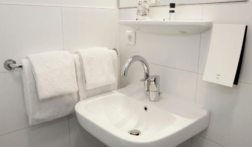 Un baño con un lavamanos blanco, dos toallas, un espejo y un dispensador de jabón.