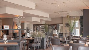 Interior modern d'un restaurant amb sostres alts, conductes a la vista i mobiliari combinat de fusta i metall.