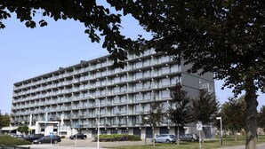 Un edifici de diversos pisos amb façana uniforme, amb balcons i una zona d'aparcament al davant.