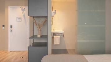 Una habitación de hotel moderna con una cama, un baño con lavamanos y perchero, y una puerta con cerradura.