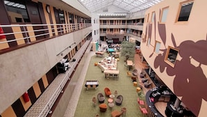A multi-level atrium with a central open space featuring tables and chairs, surrounded by balconies and a bar area. - Cowool Lille Villeneuve D'Ascq - Ex Olivarius (Villeneuve-d'Ascq)