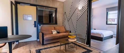 A modern room with a sofa, a small round table, a patterned rug, and a bed with a view.