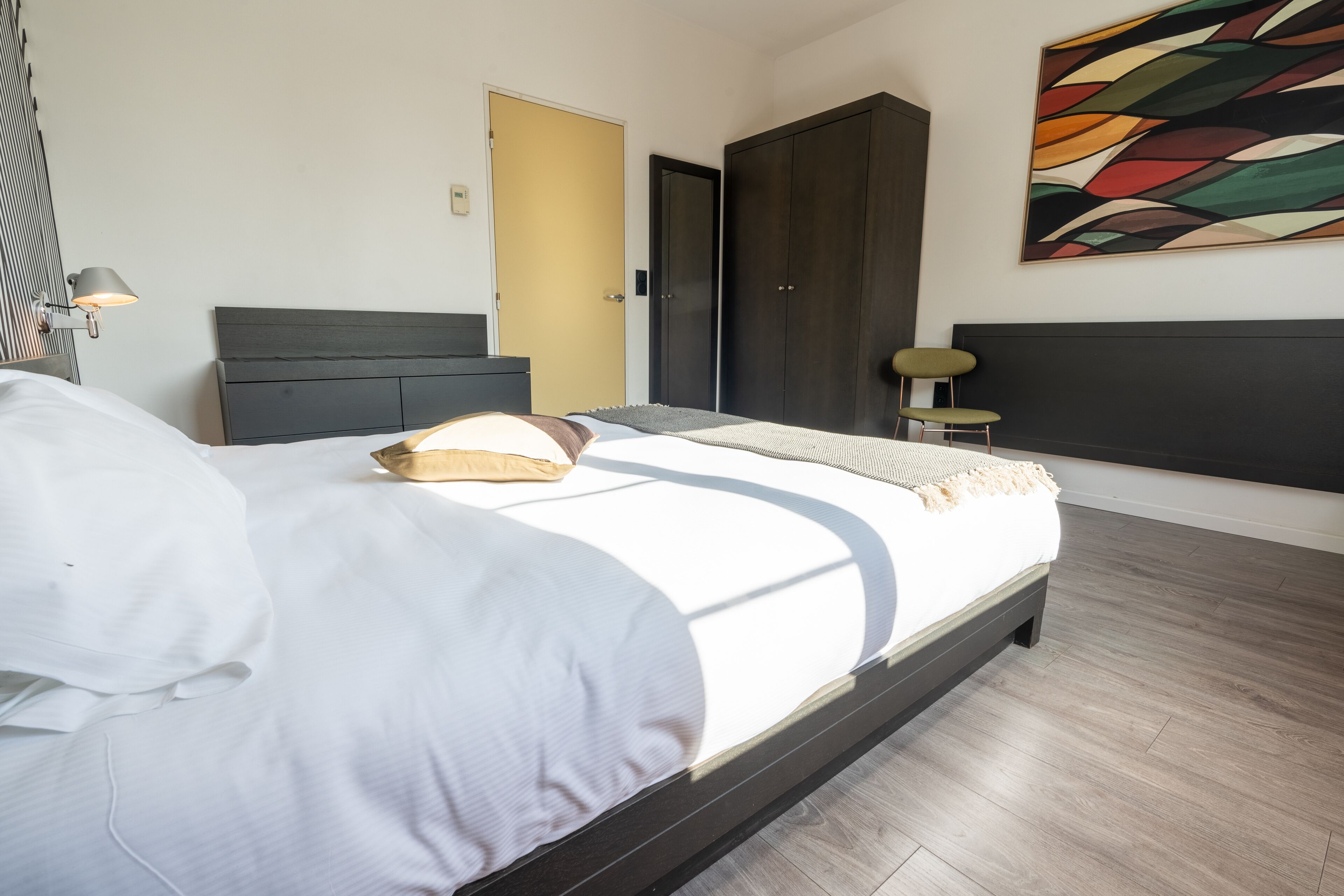 A modern bedroom with a large bed, a wardrobe, and a painting on the wall.