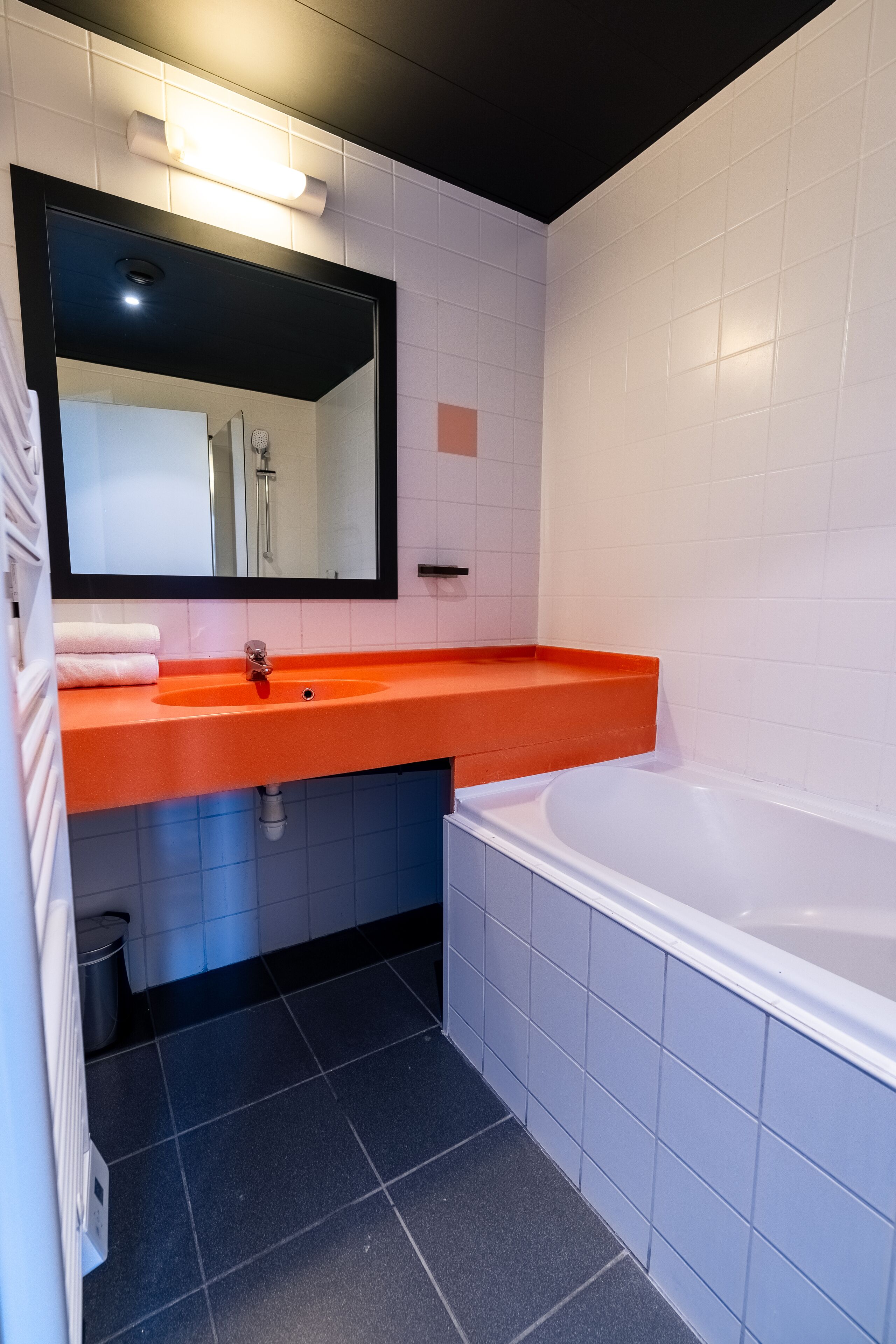 A modern bathroom with a white sink, orange countertop, and a large bathtub.