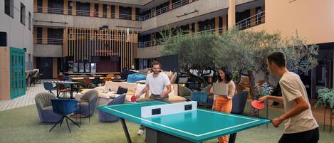 A spacious indoor area with a ping pong table, seating, and a high ceiling with skylights.