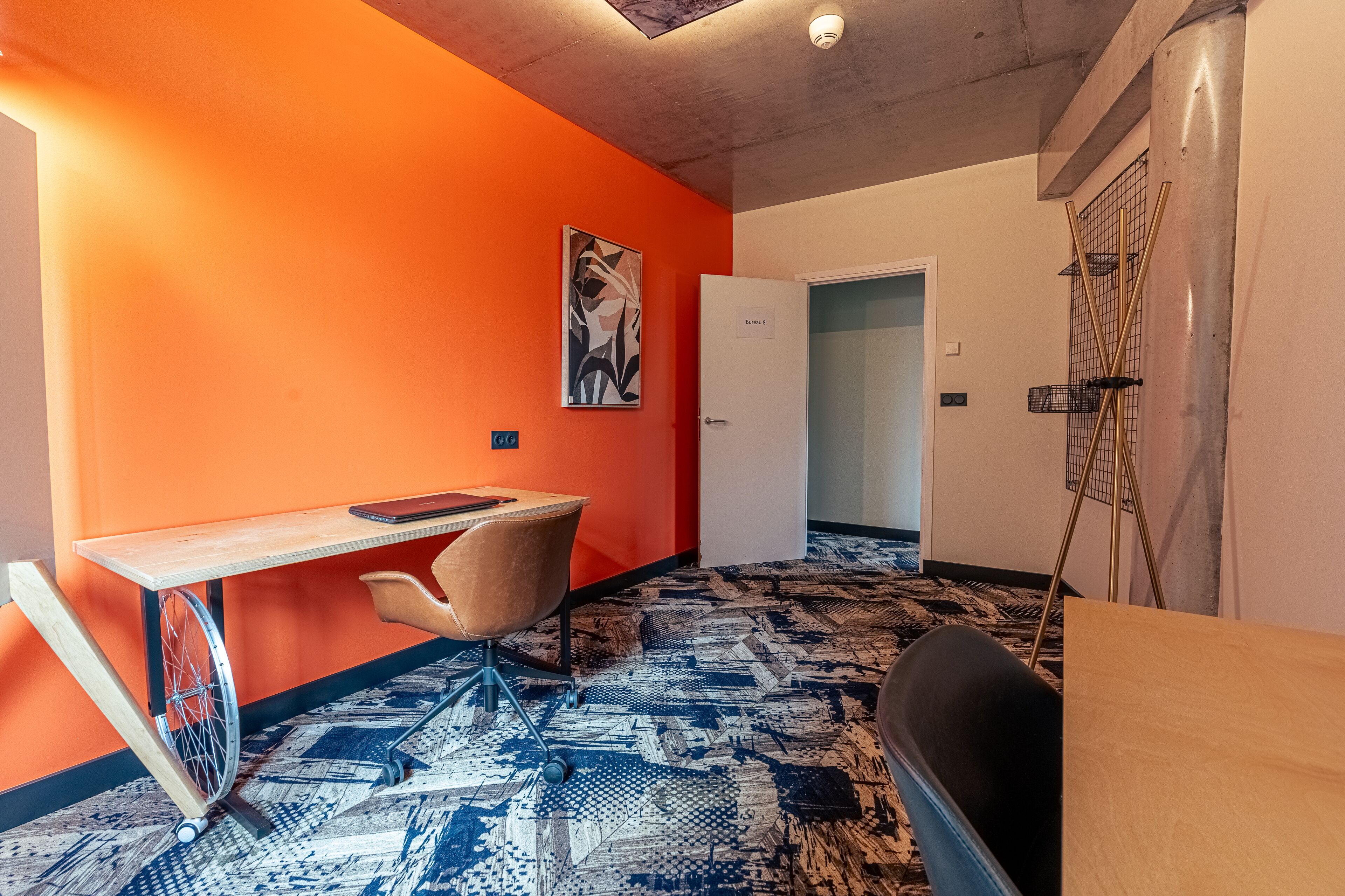 A room with a wheelchair-accessible desk, a chair, a patterned carpet, and a door labeled "Bedroom 8".