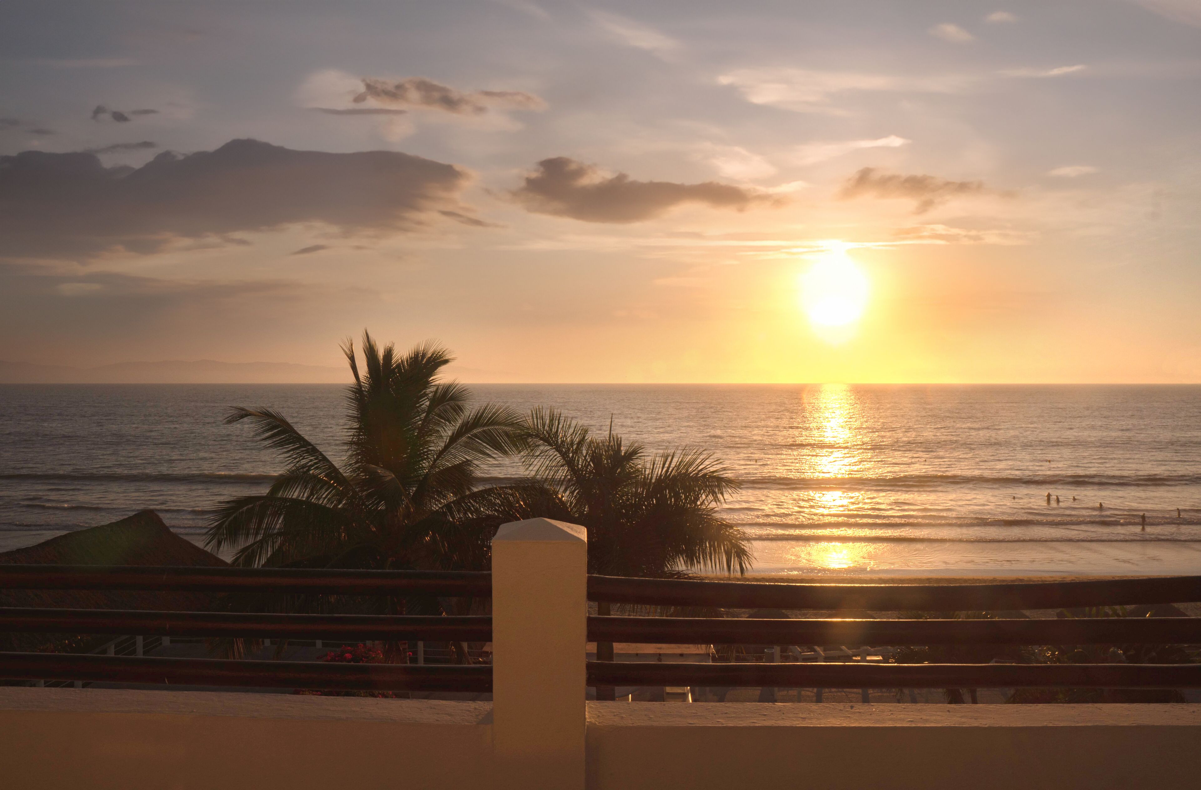 A sunset over the ocean with palm trees and a beach in the foreground.