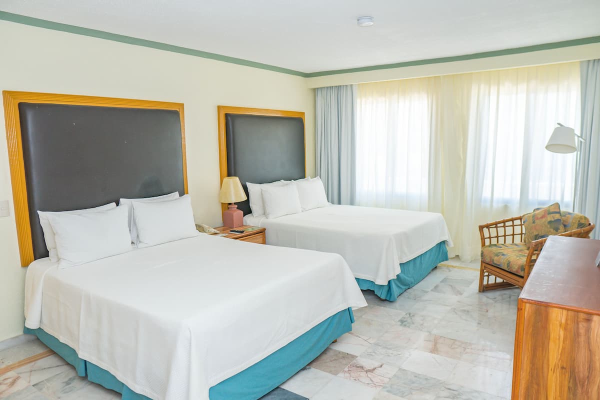 Habitación de hotel con dos camas, una silla, un escritorio y una lámpara.