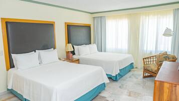 Habitación de hotel con dos camas, una silla, un escritorio y una lámpara.