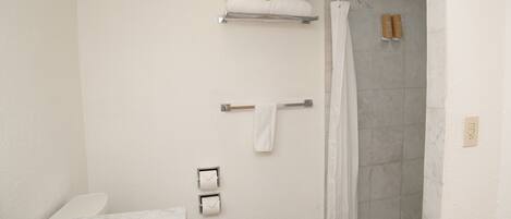 Un baño con inodoro, lavamanos, ducha con puerta de vidrio y toalleros.