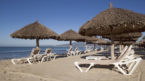 A beach with thatched umbrellas and white lounge chairs arranged along the shoreline. - Samba Vallarta - All Inclusive (Nuevo Nayarit)