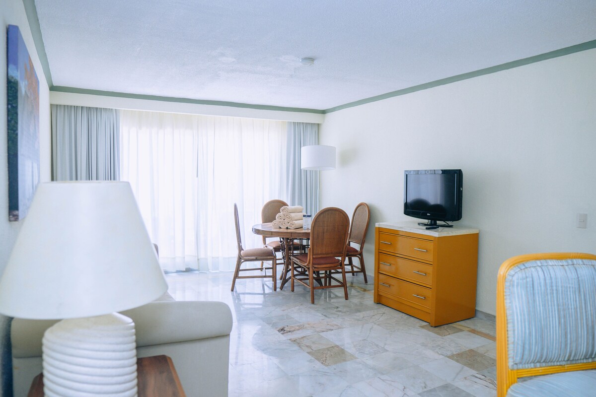 Ein Hotelzimmer mit Esstisch, Stühlen, Fernseher, Sofa, Lampe und Bett.