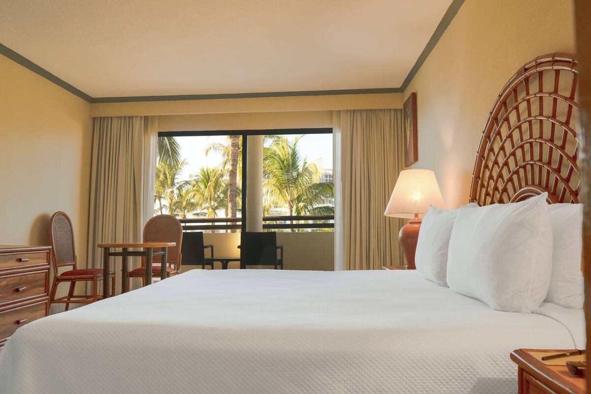 Habitación de hotel con una cama grande, un escritorio, una silla, un televisor y una ventana con cortinas.