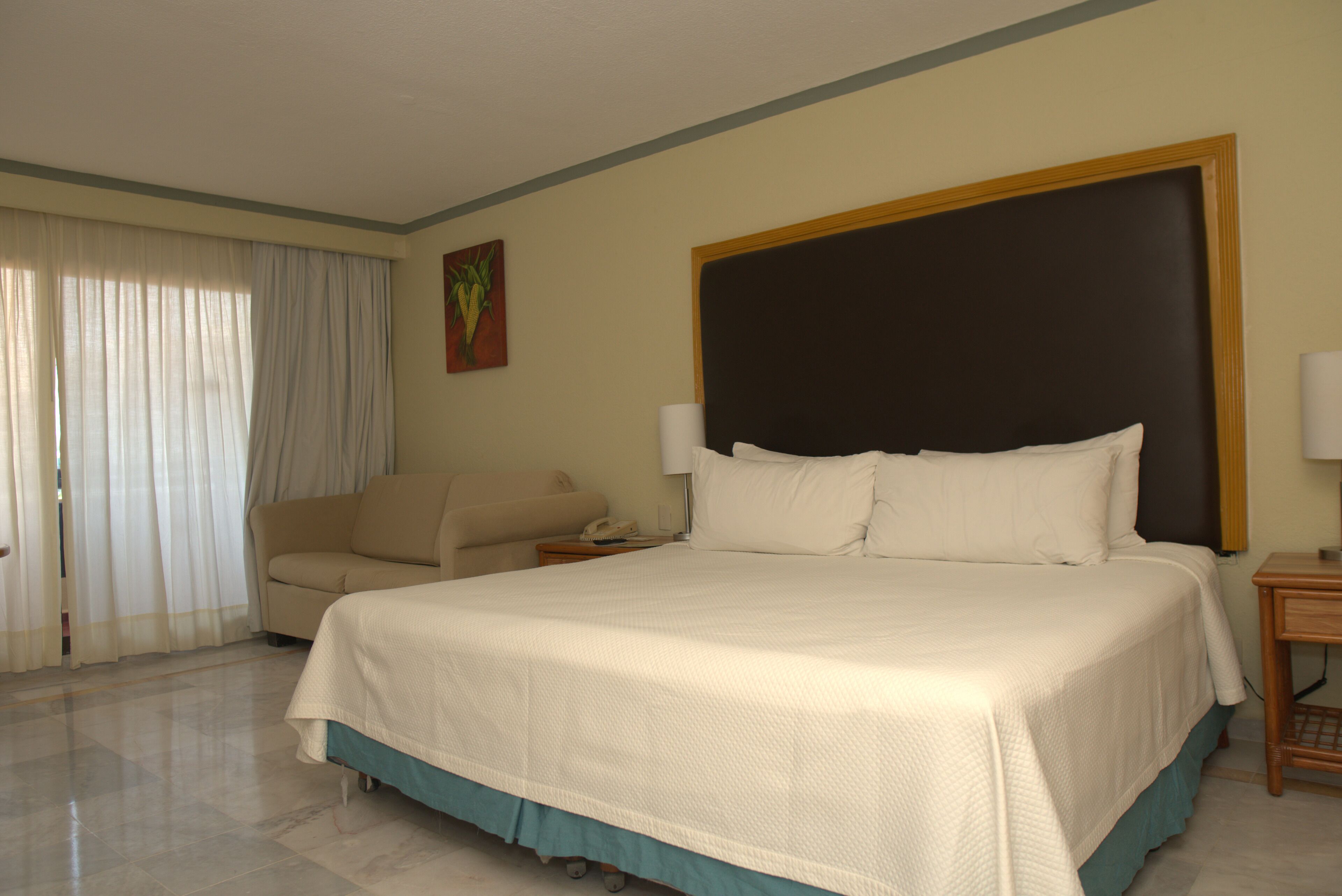 A hotel room with a bed, a chair, a nightstand, and a painting on the wall.