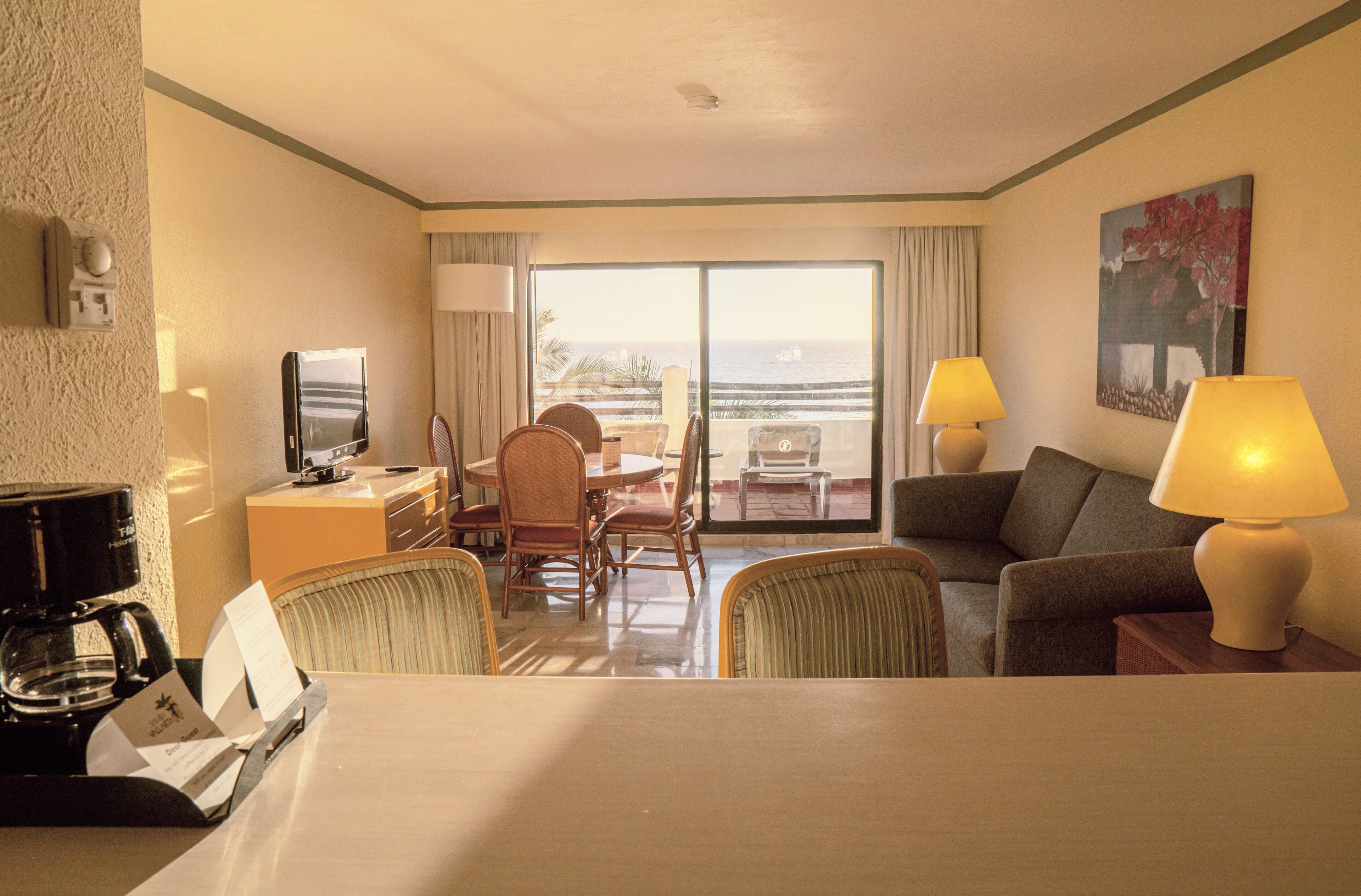 Habitació d'hotel amb zona de menjador, sofà, dues làmpades, televisió i vista a l'oceà.