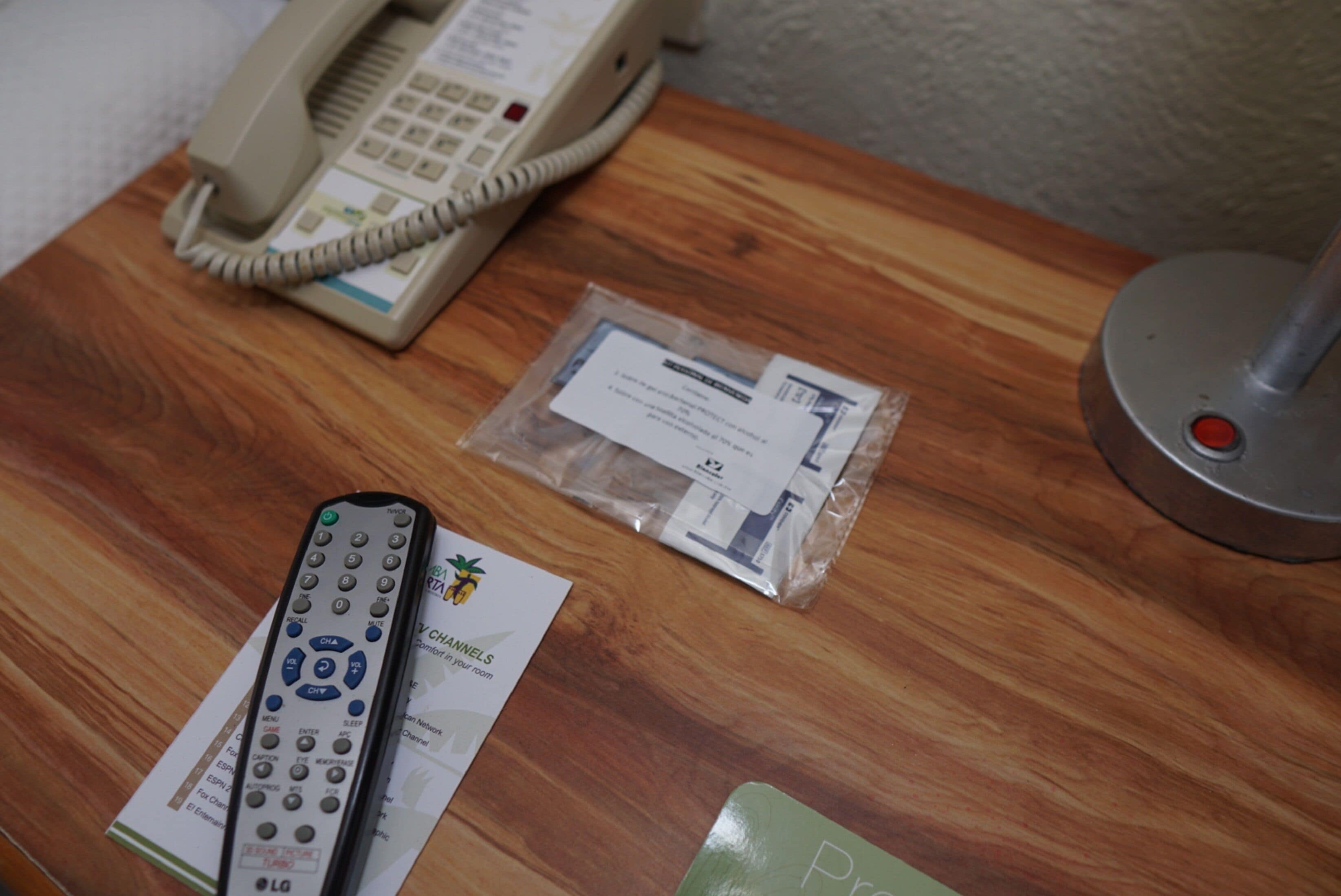 Una mesa de madera con un teléfono, un control remoto y un pequeño folleto.