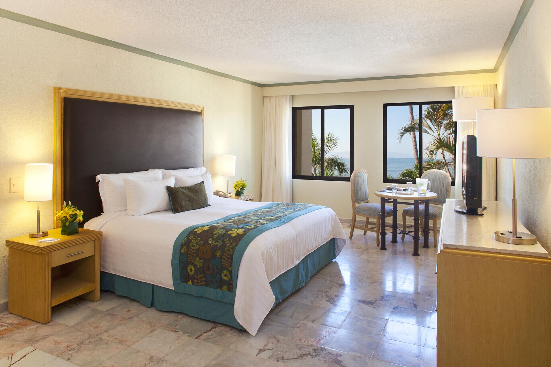A hotel room with a bed, bedside tables, a desk, a chair, and a TV.
