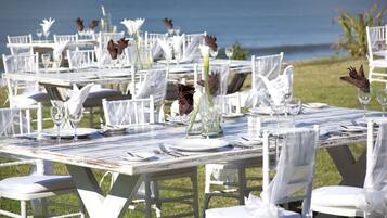 Outdoor dining tables set up with white chairs, white tablecloths, and floral centerpieces.