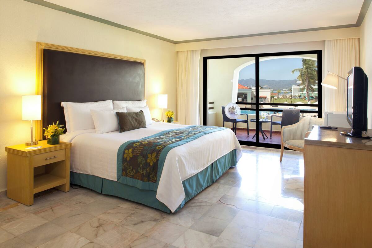 Habitación de hotel con una cama grande, un escritorio, una silla y vistas al exterior.