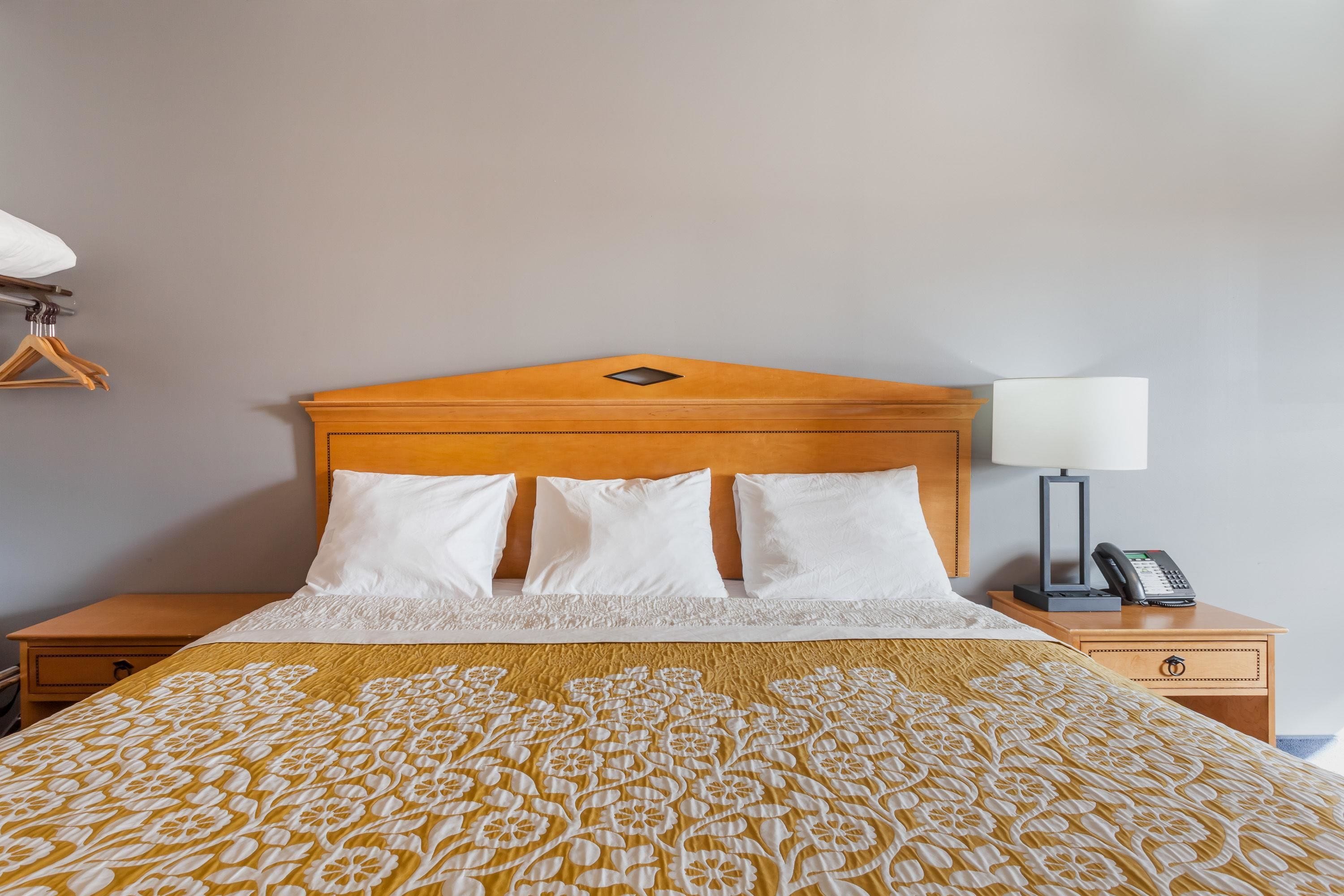 A neatly made bed with a patterned bedspread, a wooden headboard, and a bedside table with a lamp and phone.