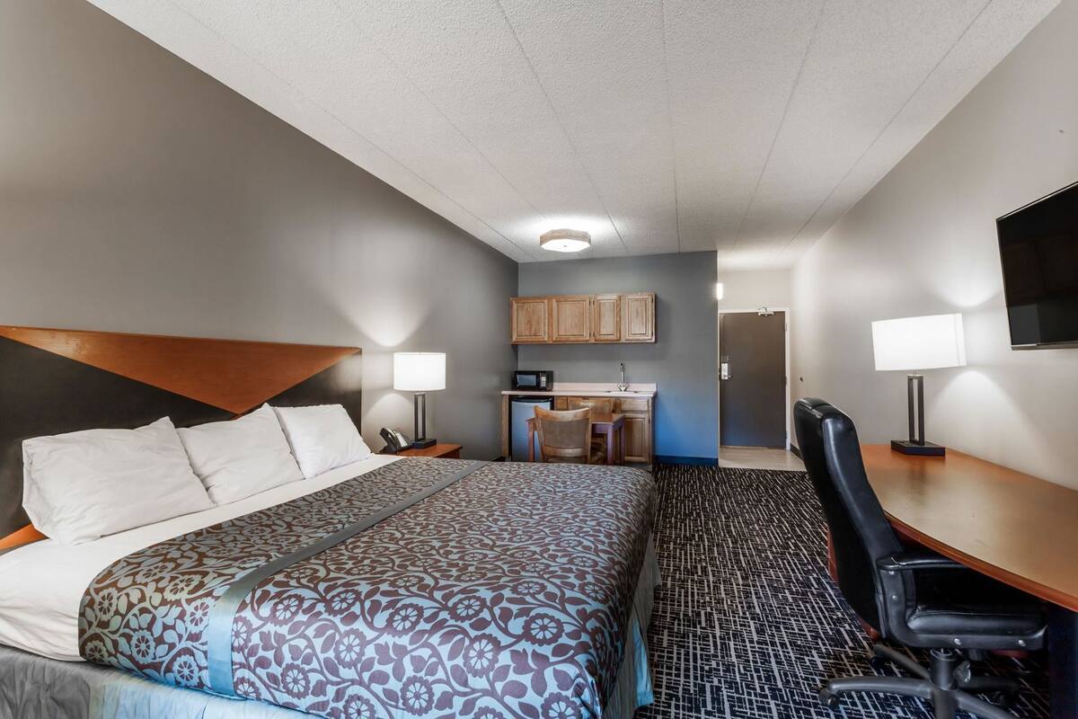 Ein Hotelzimmer mit Bett, Schreibtisch, Stuhl, Küchenzeile und Fernseher.
