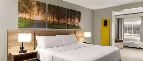 Una habitación de hotel con una cama grande, dos mesitas de noche con lámparas, un cabecero, una ventana con cortinas y tres cuadros colgados en la pared.