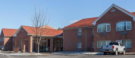 A multi-story brick building with a red roof, a white pickup truck parked in front, and a clear blue sky.