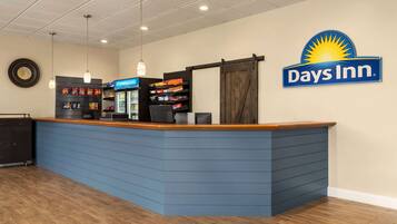 A reception area with a blue counter, a Days Inn sign, a refrigerator, and a snack shelf.
