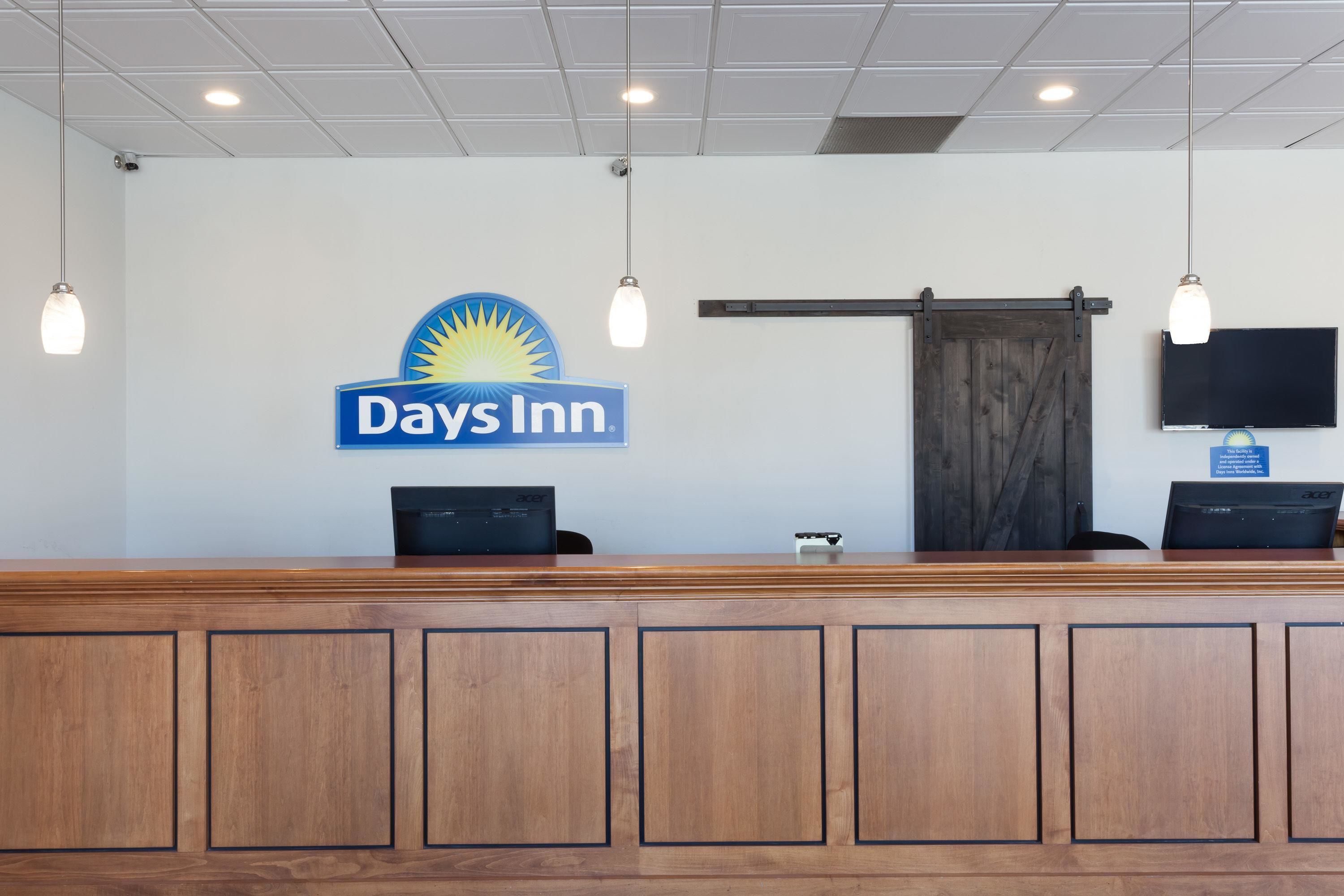 A reception desk with a Days Inn sign, a wooden counter, two computer monitors, and a mounted television.