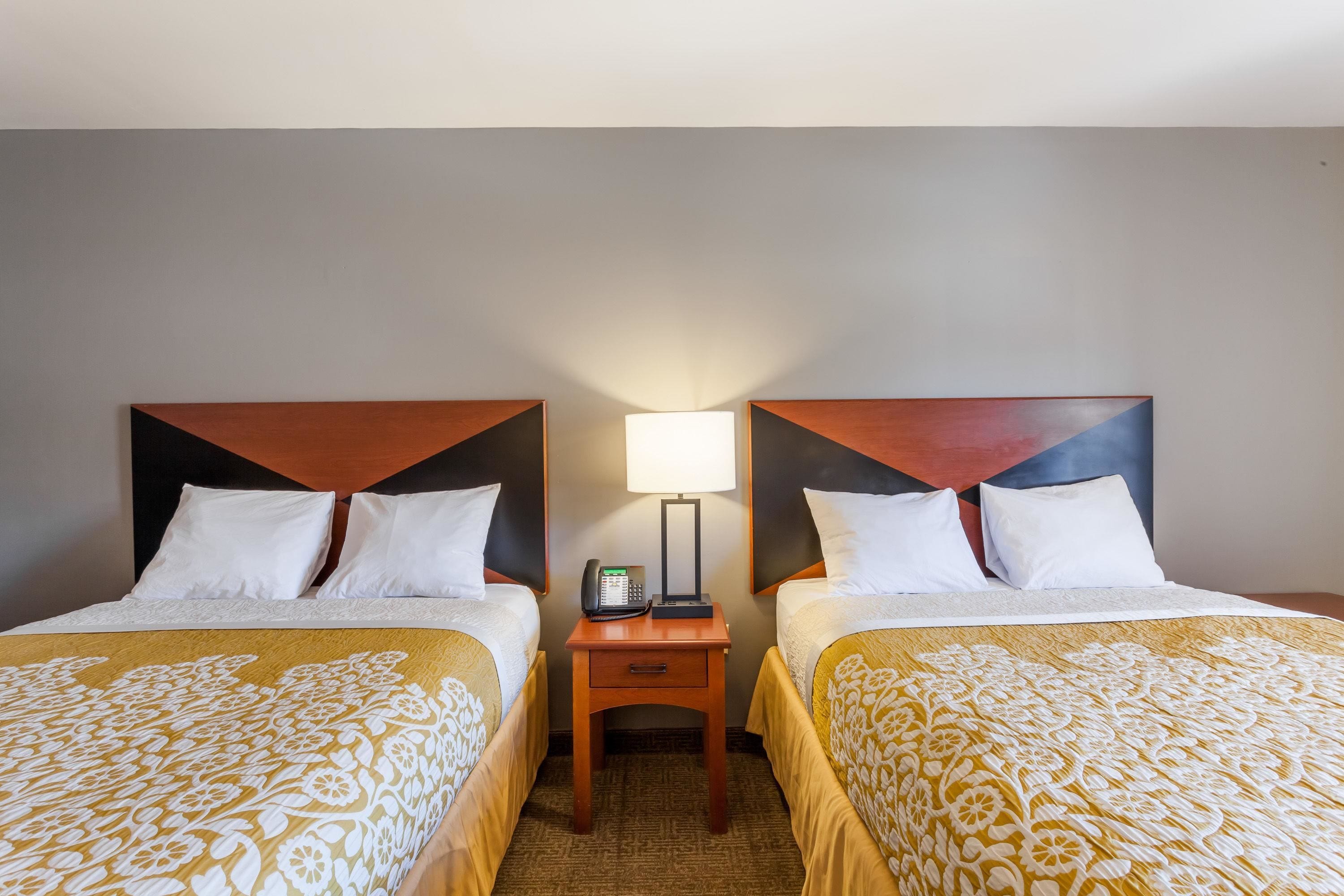 A hotel room with two beds, a bedside table with a lamp, and a phone.