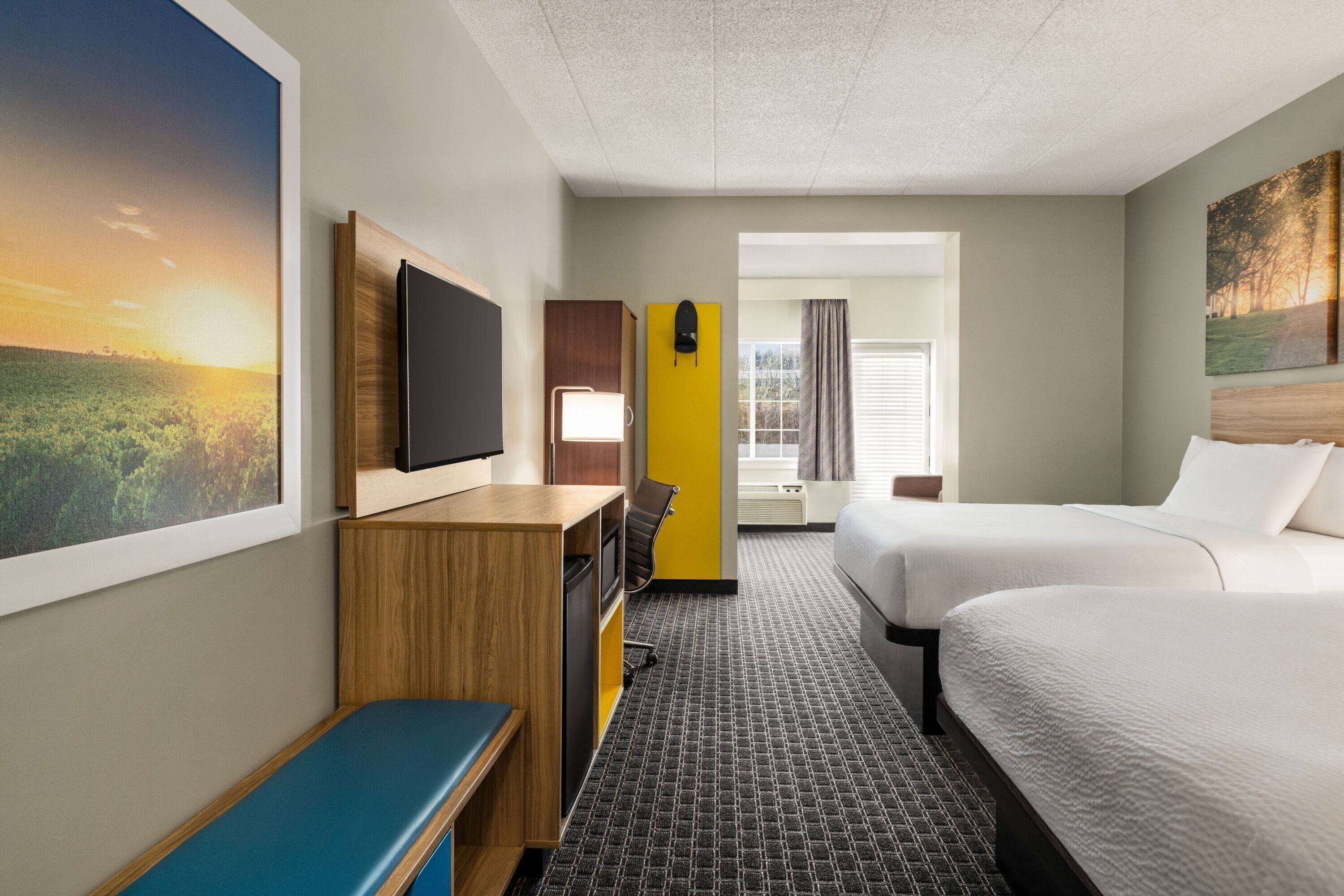 A hotel room with two beds, a desk, a chair, a television, and a large window with curtains.