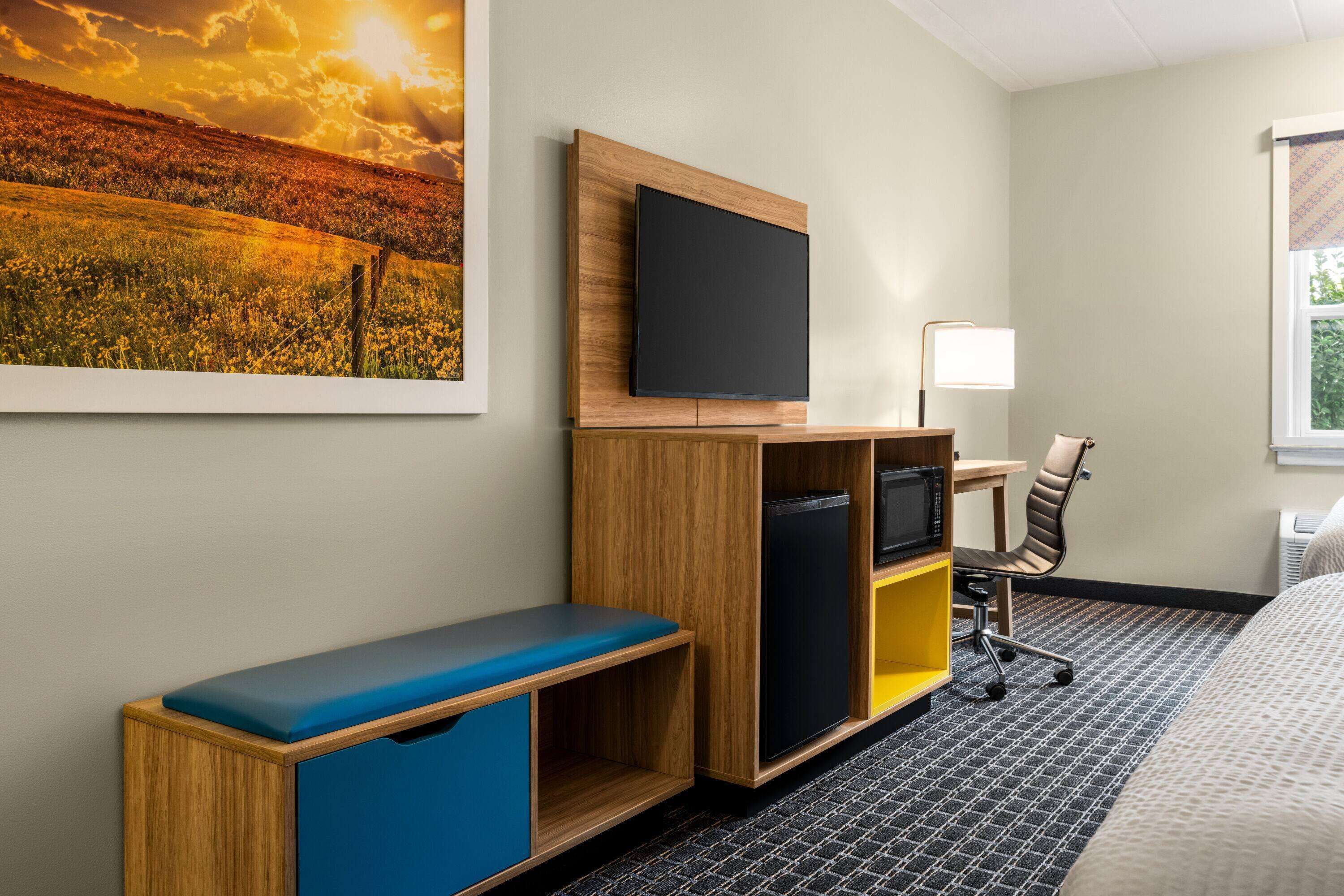 Una habitación de hotel con un escritorio de madera, un televisor de pantalla plana, un banco, una silla y una cama.