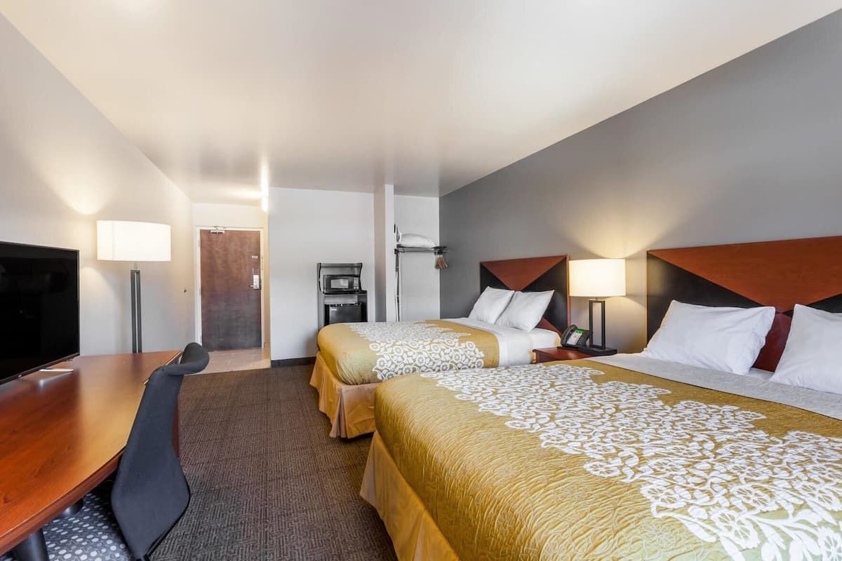 Ein Hotelzimmer mit zwei Betten, einem Schreibtisch, einem Fernseher, einer Mikrowelle und einem Telefon.