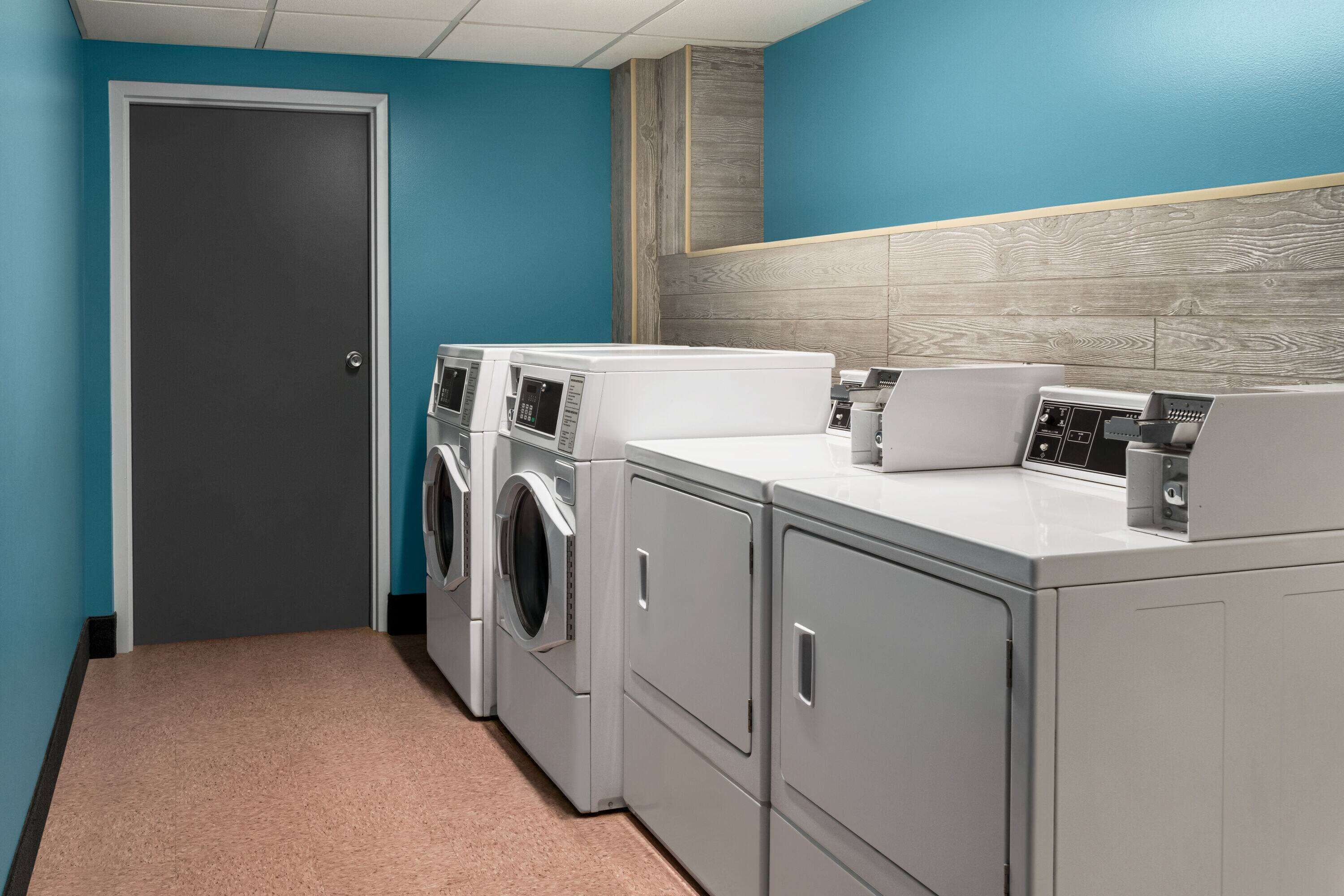 Un cuarto de lavandería con puerta, dos lavadoras, una secadora y una encimera con microondas.