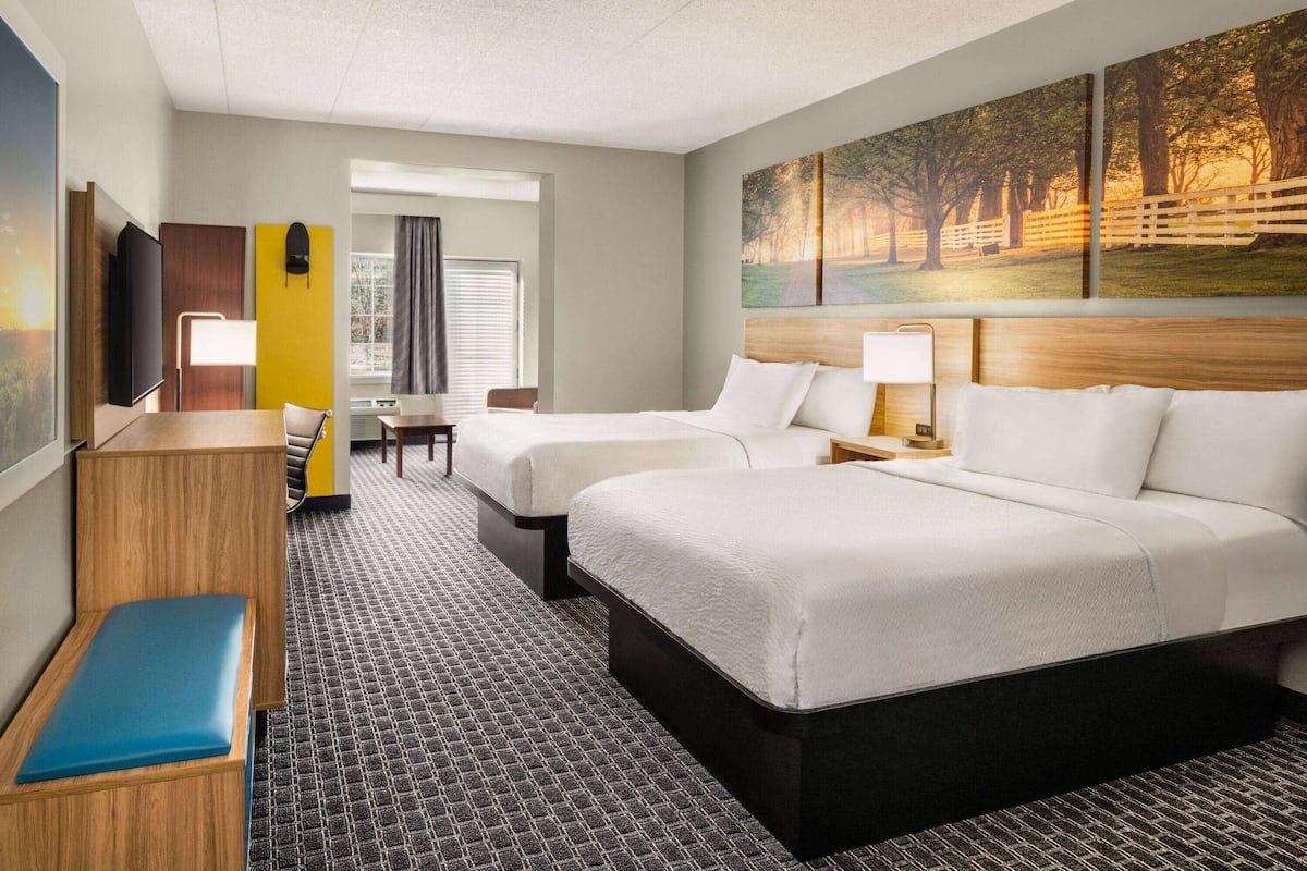 Ein Hotelzimmer mit zwei Betten, einem Schreibtisch, einem Sessel, einem Fernseher und einem Bild an der Wand.