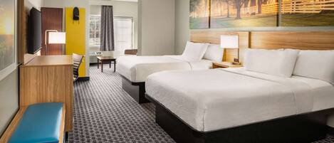 A hotel room with two beds, a desk, a chair, a TV, and a painting on the wall.