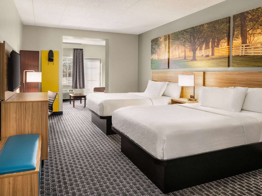 A hotel room with two beds, a desk, a chair, a TV, and a painting on the wall.