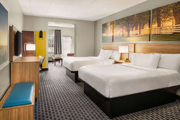 A hotel room with two beds, a desk, a chair, a TV, and a painting on the wall.