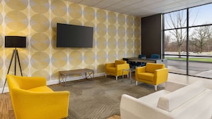 Una sala de conferencias moderna con una gran televisión de pantalla plana, un papel tapiz amarillo y blanco con diseño, y un amplio ventanal con vistas al exterior.